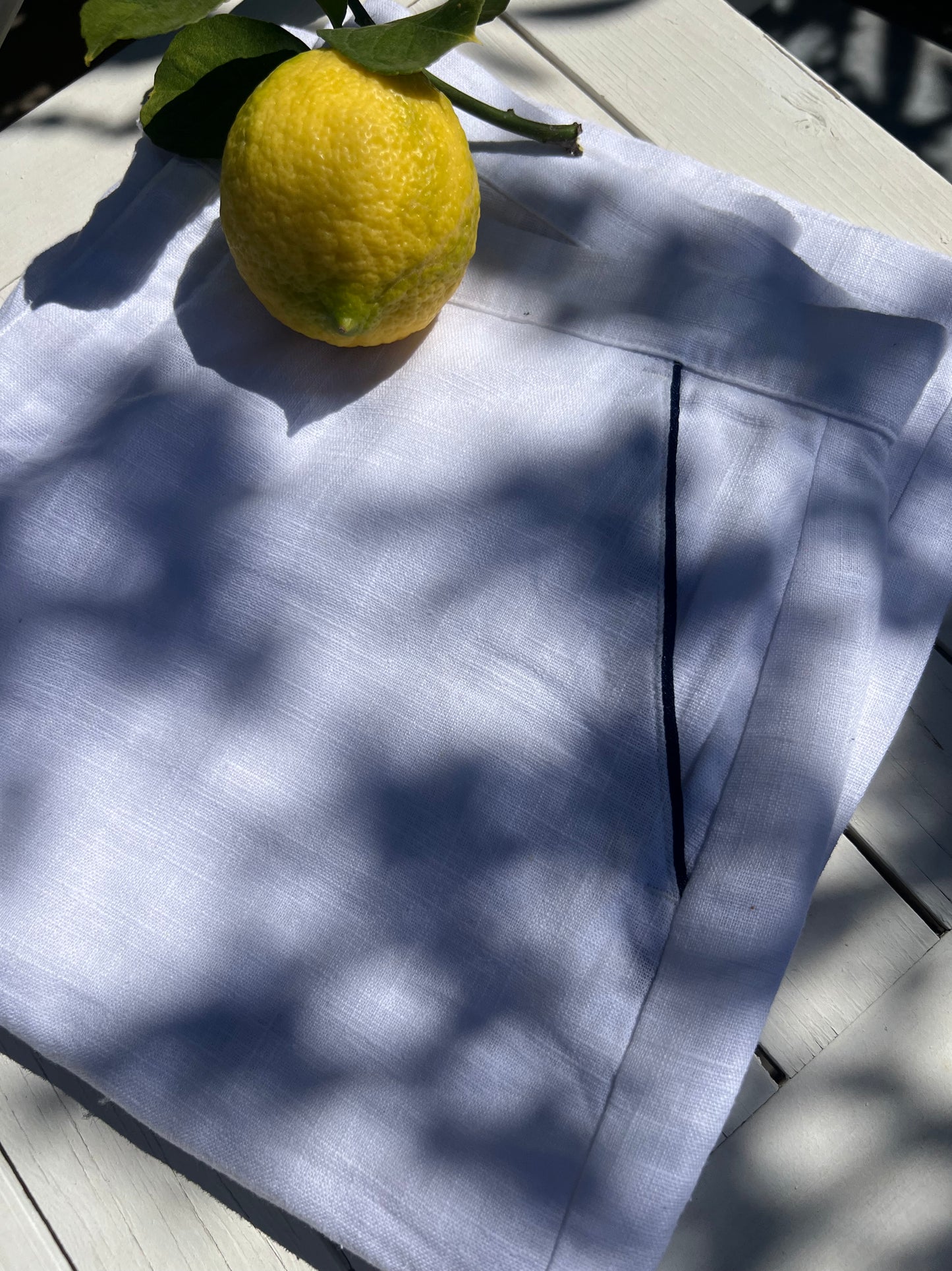 White linen trousers with navy piping on the pockets, styled on holiday, close-up image