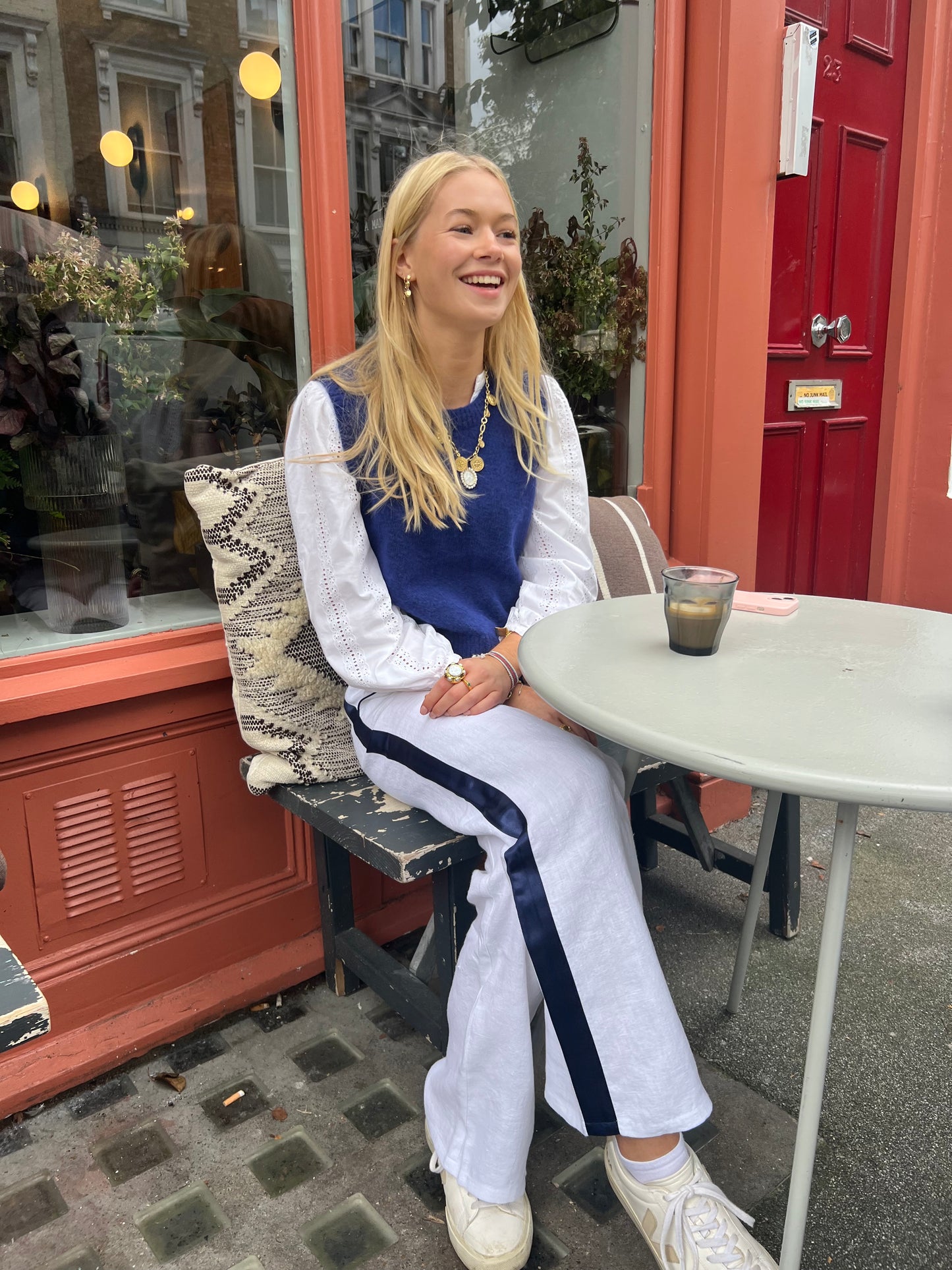 Woman wearing white linen trousers with a blue stripe, sitting at a table having a coffee