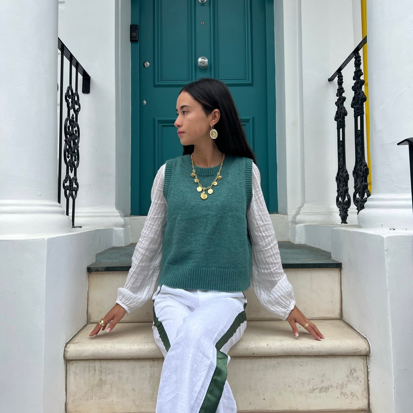 Woman wearing white linen trousers with a green stripe down the side, sitting outside a doorway